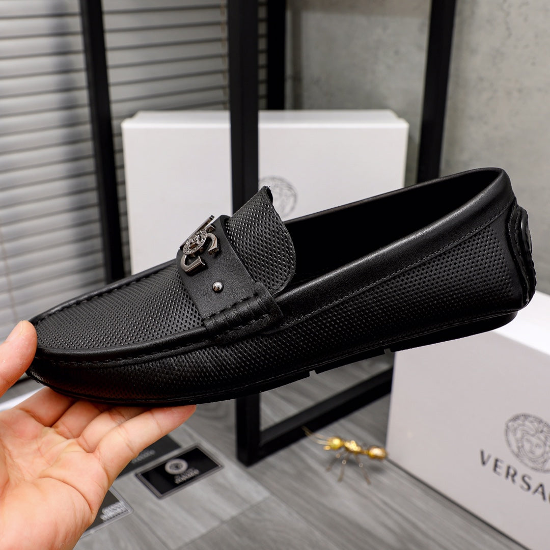 Versace black slip-on loafer held in hand, textured upper and logo buckle