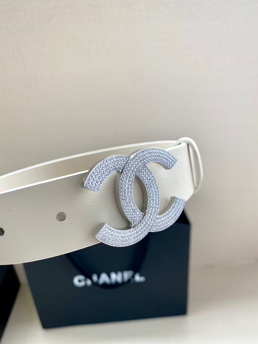 Chanel belt close-up: light cream strap with stud holes and glitter CC buckle detail