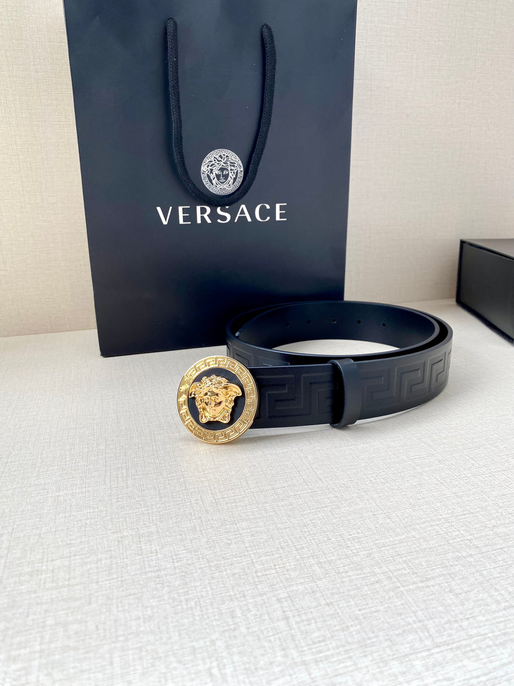 Navy Versace belt laid flat with gold lion buckle and embossed Greca design
