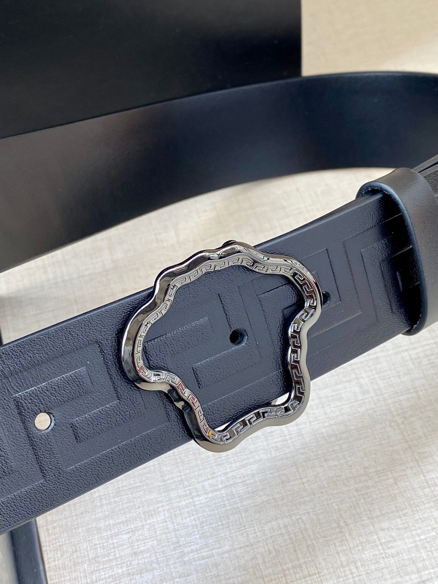 Close-up designer belt in dark navy with embossed texture and silver ornate buckle