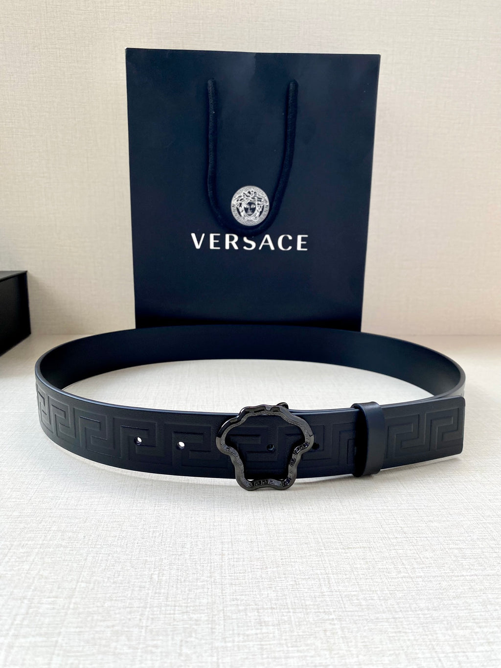 Designer belt laid flat in dark navy with embossed pattern and silver buckle