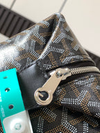 Close-up of zipper pull and logo plate on patterned canvas with black leather trim