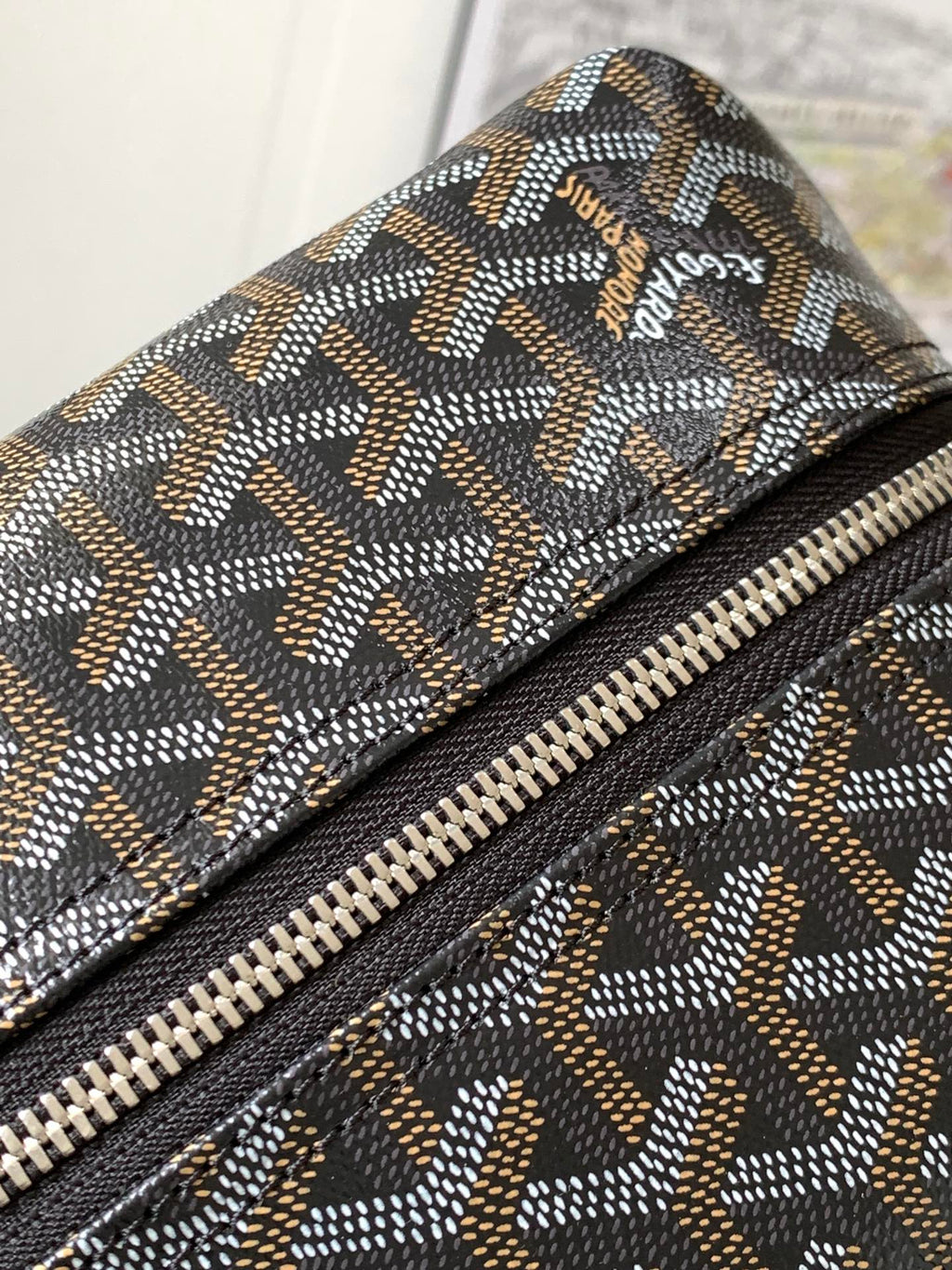 Close-up of patterned canvas with zipper track and small brown logo patch