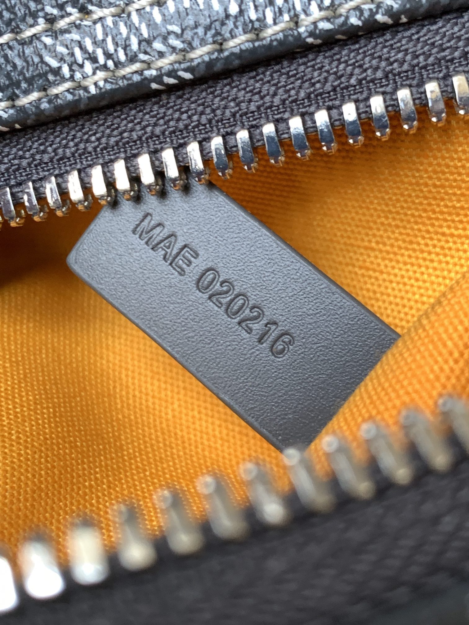 Orange lining leather tag stamped 'MADE 2022' under silver zipper teeth
