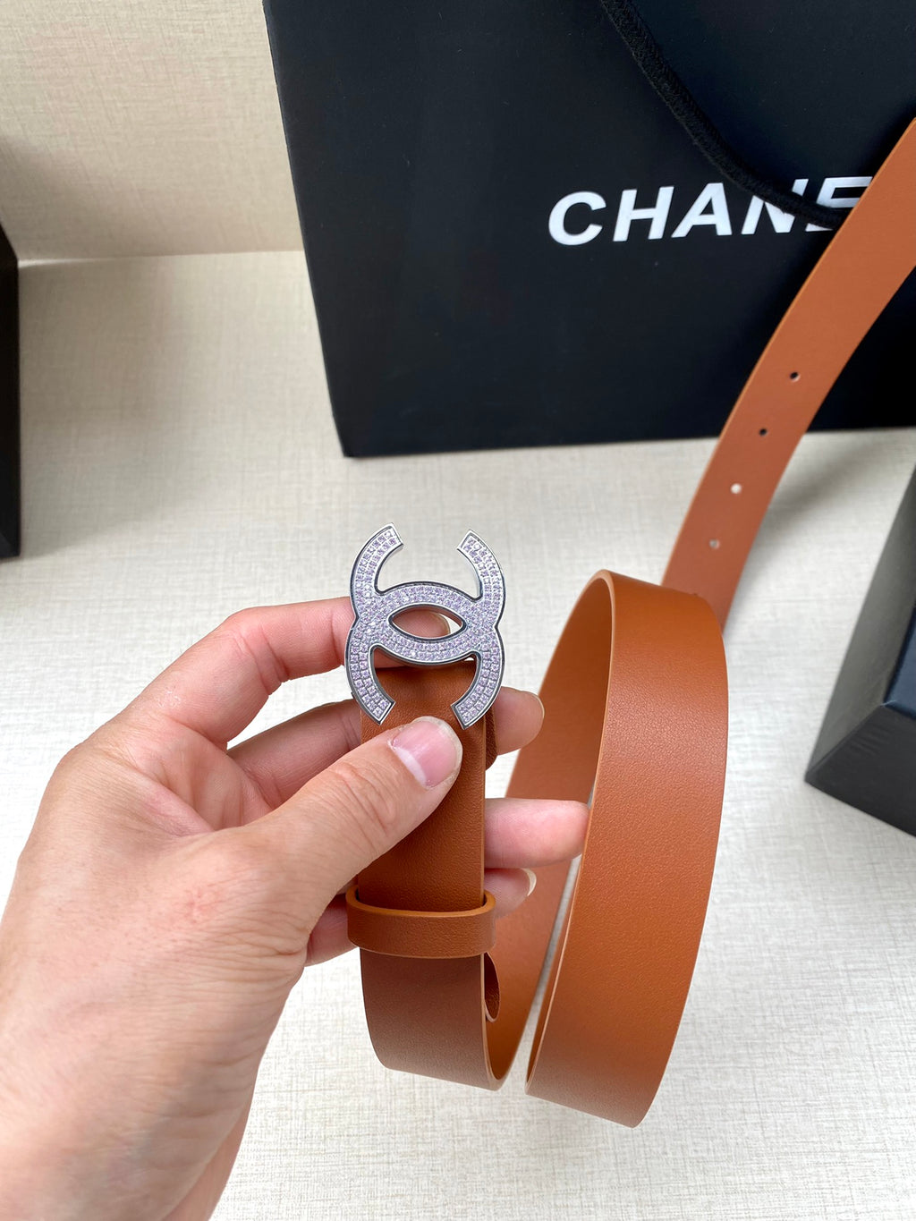 Tan leather belt with CC logo buckle, side view showing belt holes