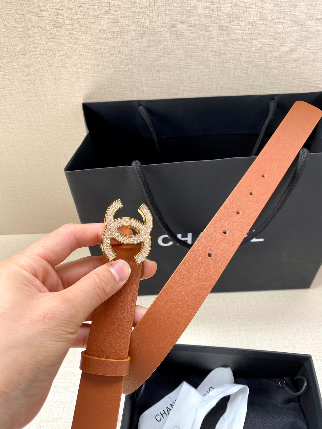 Tan leather belt with gold-tone CC logo buckle and visible strap holes