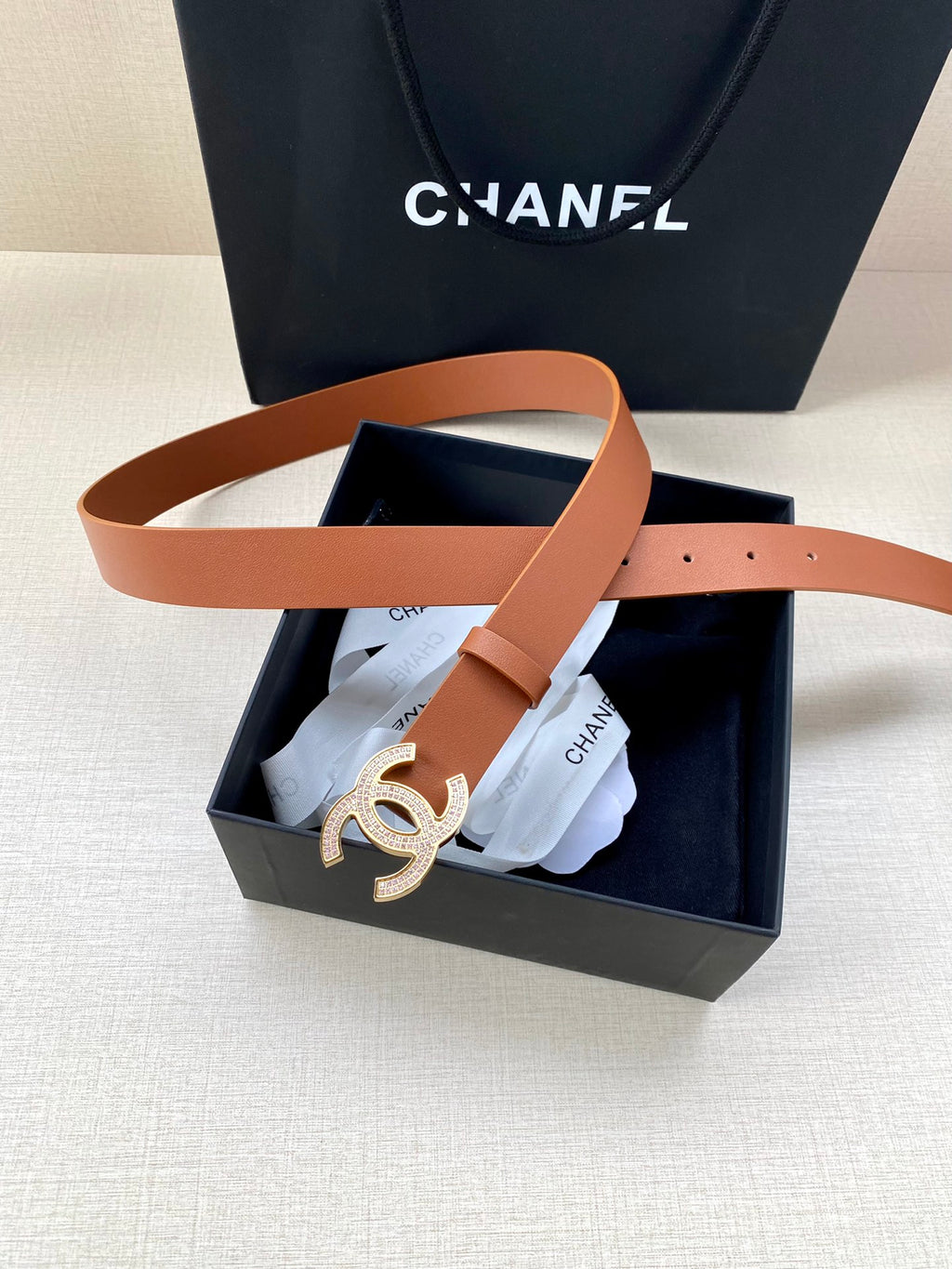 Tan leather belt with gold-tone CC logo buckle, partly inside the box