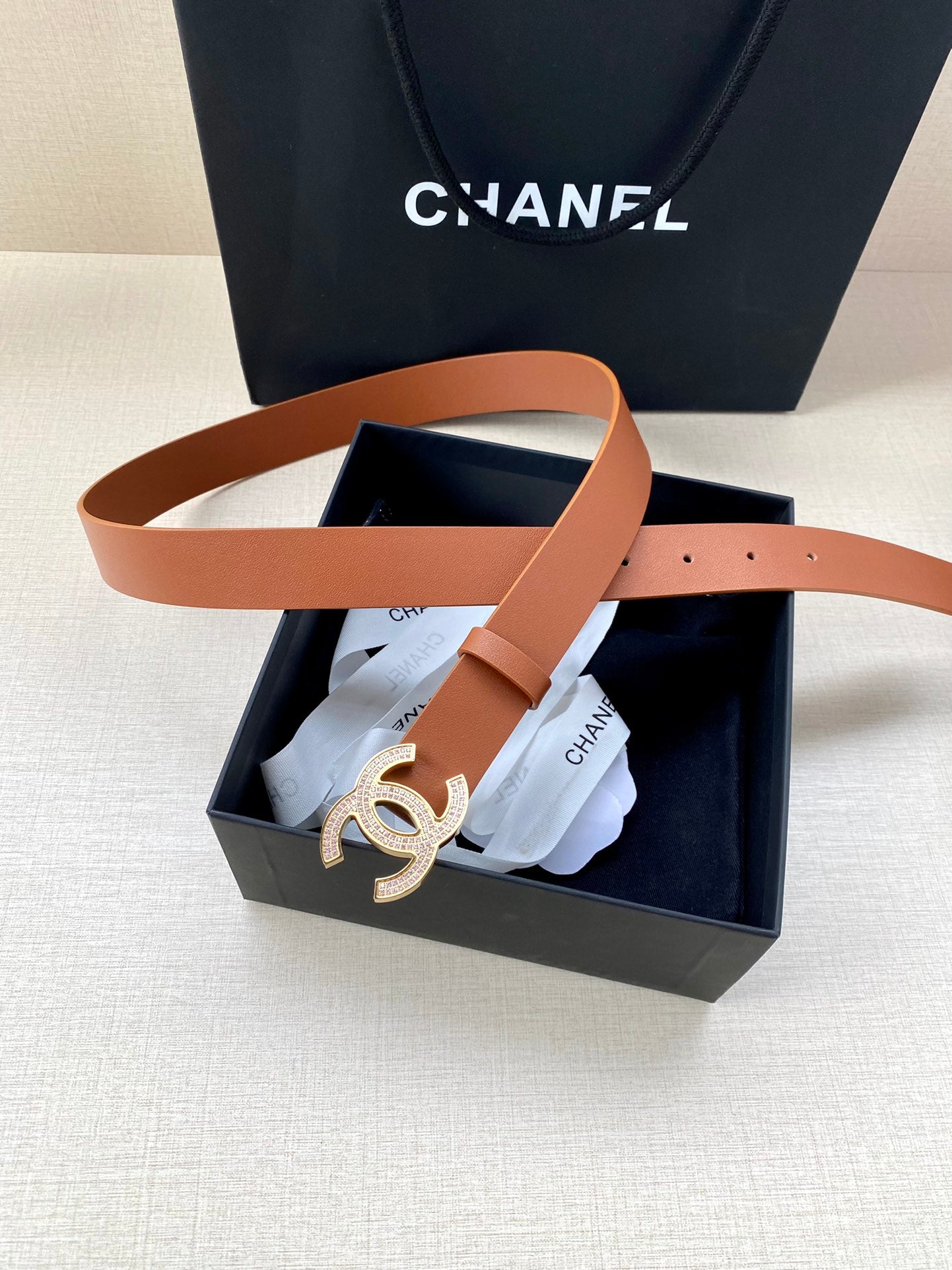Tan leather belt with gold-tone CC logo buckle, partly inside the box