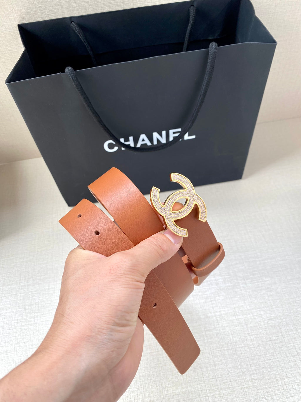 Tan leather belt with gold-tone CC logo buckle, held by hand with tips