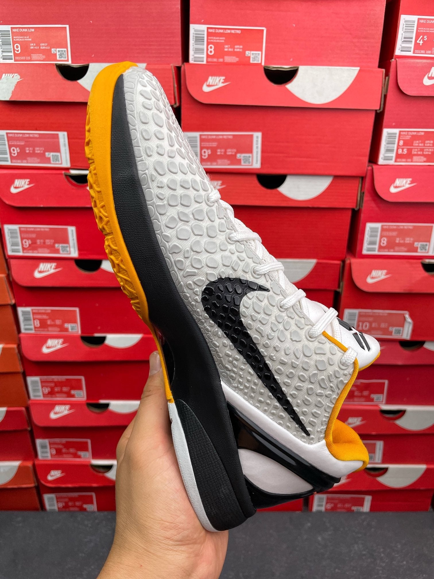 Side view of white athletic sneaker with yellow outsole edge, black sole, textured upper