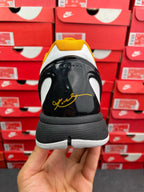 Back view of white athletic sneaker with black heel, yellow signature, gray midsole