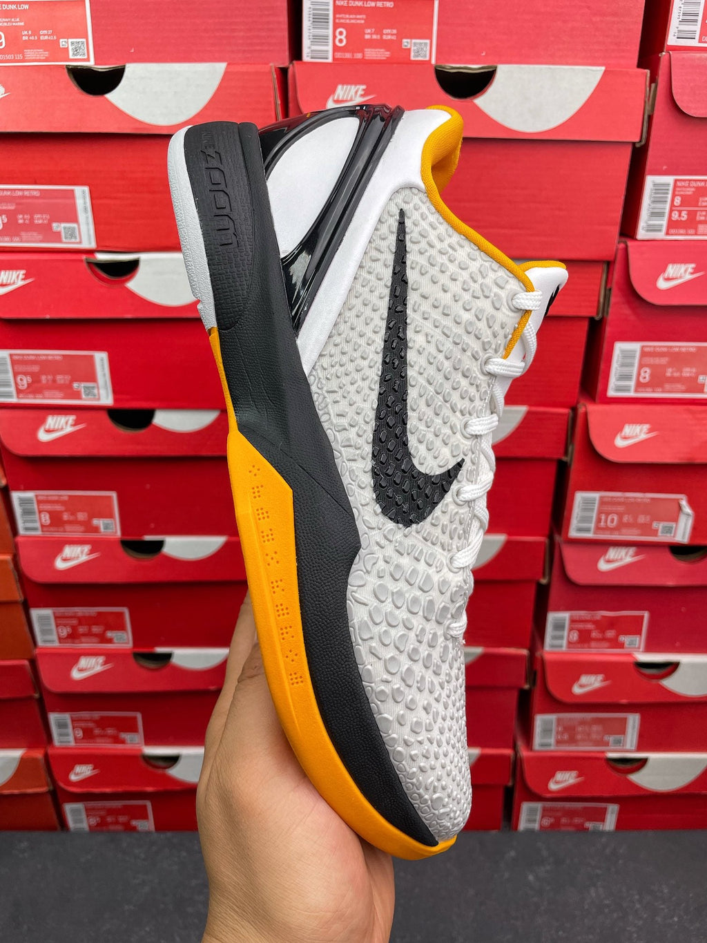 White athletic sneaker with black heel panel, yellow collar trim, textured upper, white laces