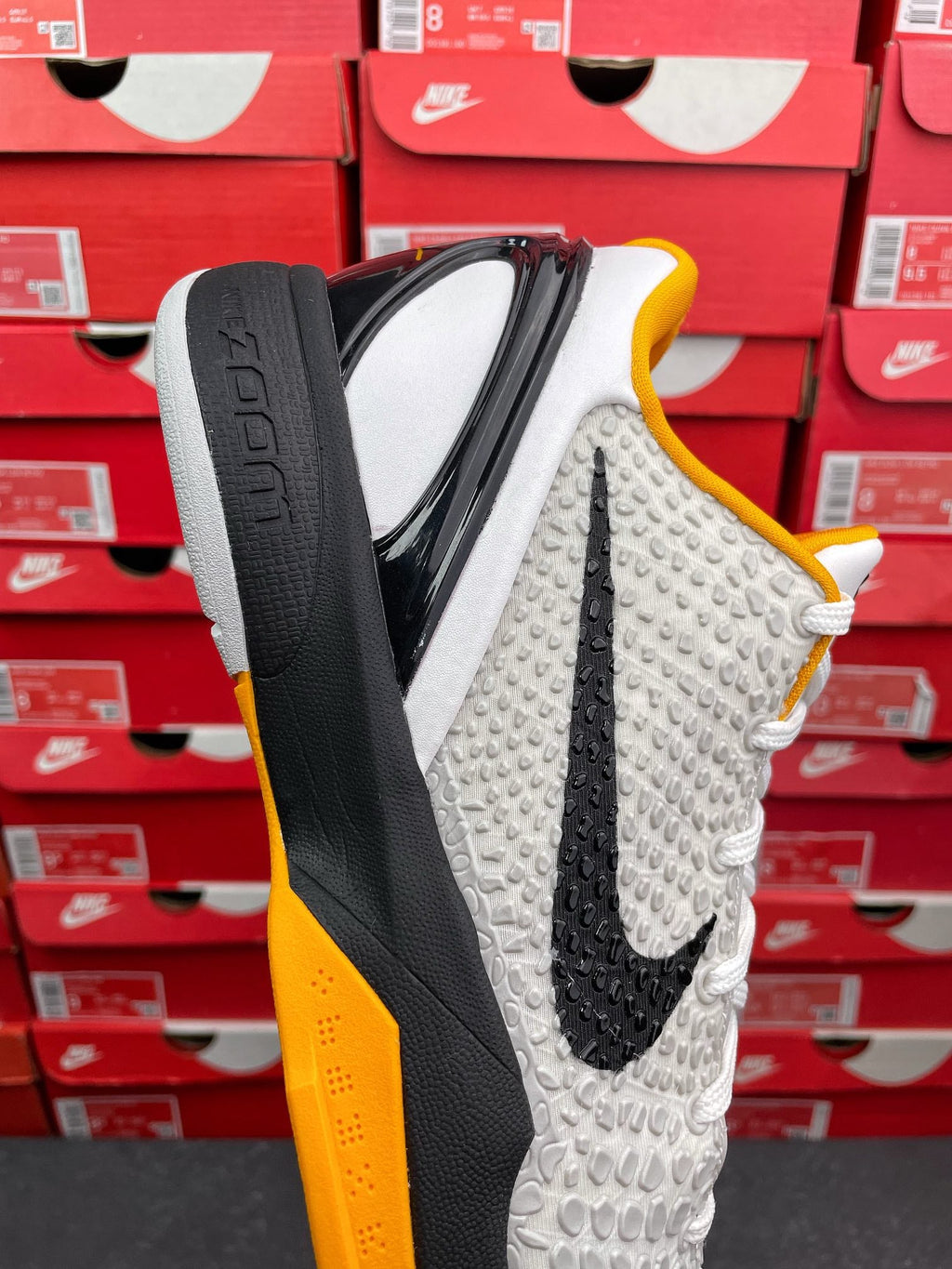 White athletic sneaker showing black side panel, yellow collar, textured knit, white laces