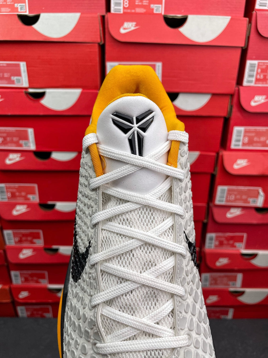 White athletic sneaker with yellow tongue, white laces, black side stripe detail