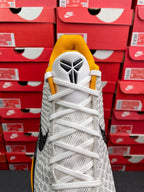 White athletic sneaker with yellow tongue, white laces, black side stripe detail