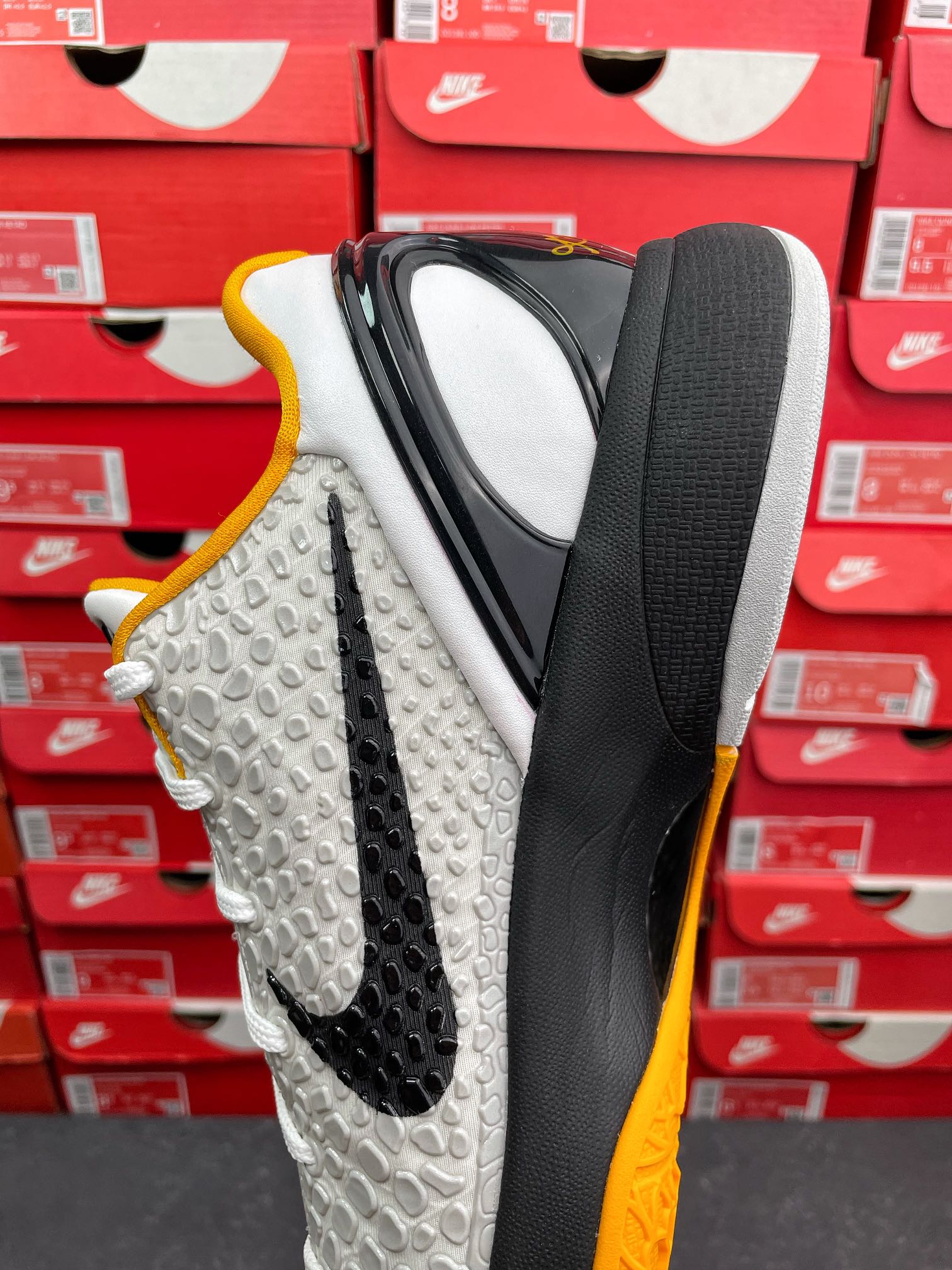 White athletic sneaker with black sidewall, yellow edge, textured upper, white laces