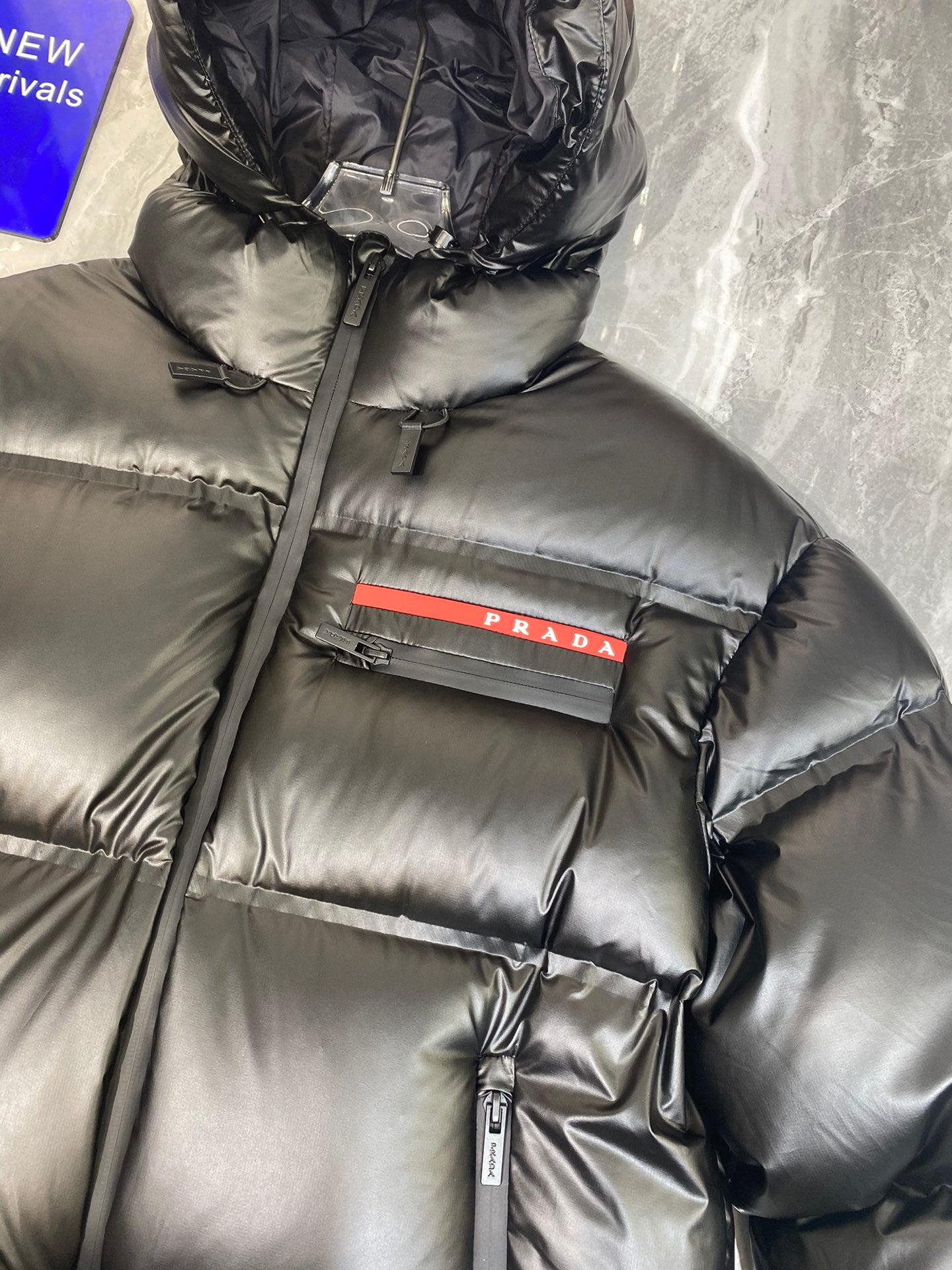 Black long puffer jacket with hood, red Prada logo stripe, and vertical zip detail