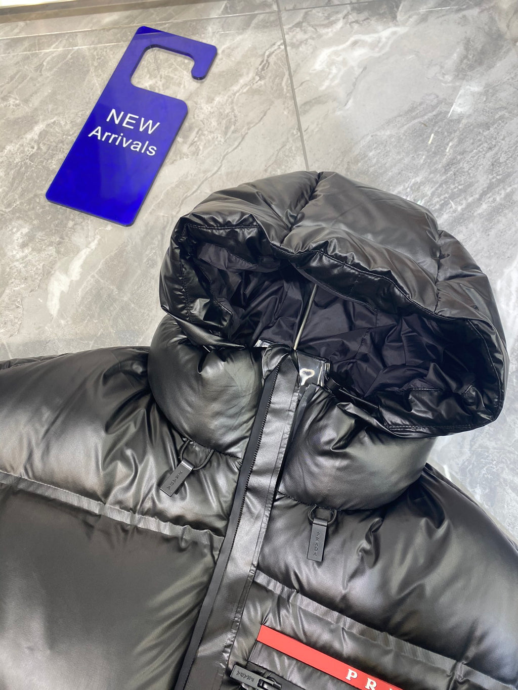 Black long puffer jacket with hood and front zip, red Prada logo patch