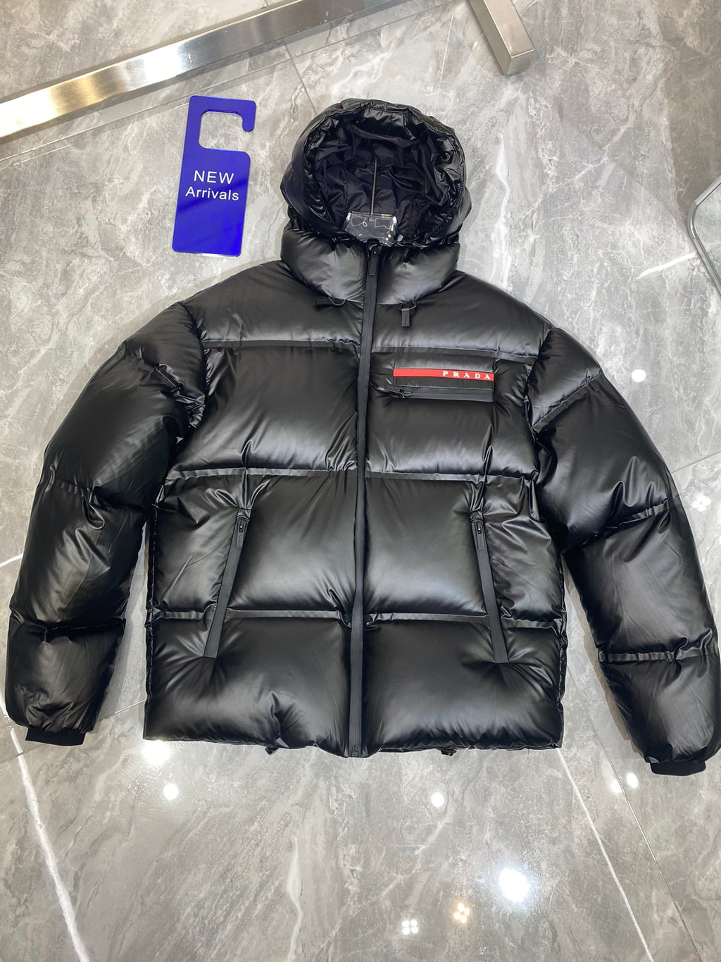 Black long puffer jacket with hood and front zip, quilted panels with Prada logo stripe