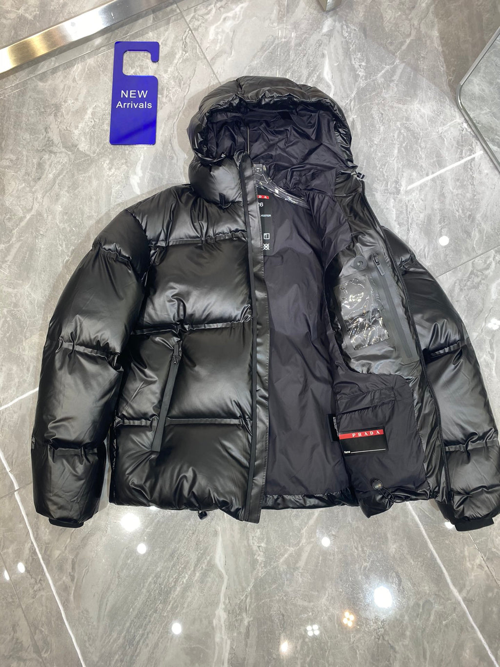 Black long puffer jacket with hood and front zip, quilted design and logo patch