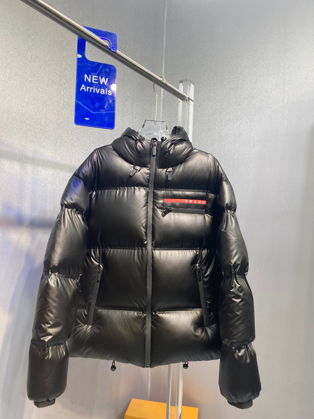 Black long puffer jacket with hood, zip front, and Prada logo patch on chest