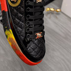 Close-up of black lace-up sneaker with gold buckle detail and red/yellow edge