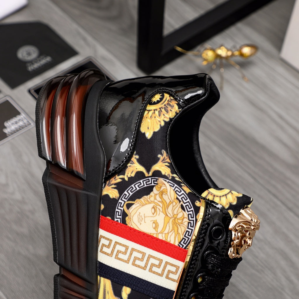 Versace luxury sneakers close-up, black patent with gold shield and red/white stripe panel.