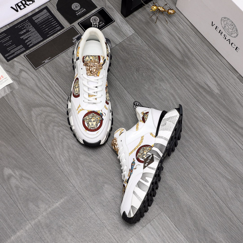 Pair of white sneakers with gold Medusa emblems, patterned accents, and tread sole