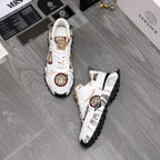 Pair of white sneakers with gold Medusa emblems, patterned accents, and tread sole