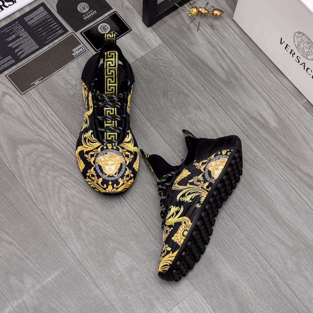 Pair of black luxury sneakers with gold baroque print and Greca logo on tongue, side view