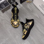 Pair of black luxury sneakers with gold baroque print and Greca logo on tongue, side view