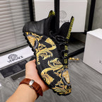 Black luxury sneakers with gold baroque fabric, Greca trim, and lace-up front, handheld