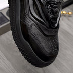 Black sneaker side view with perforated leather paneling and sculpted sole.