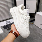 White Versace sneakers held in hand, side profile with sculpted sole and laces.