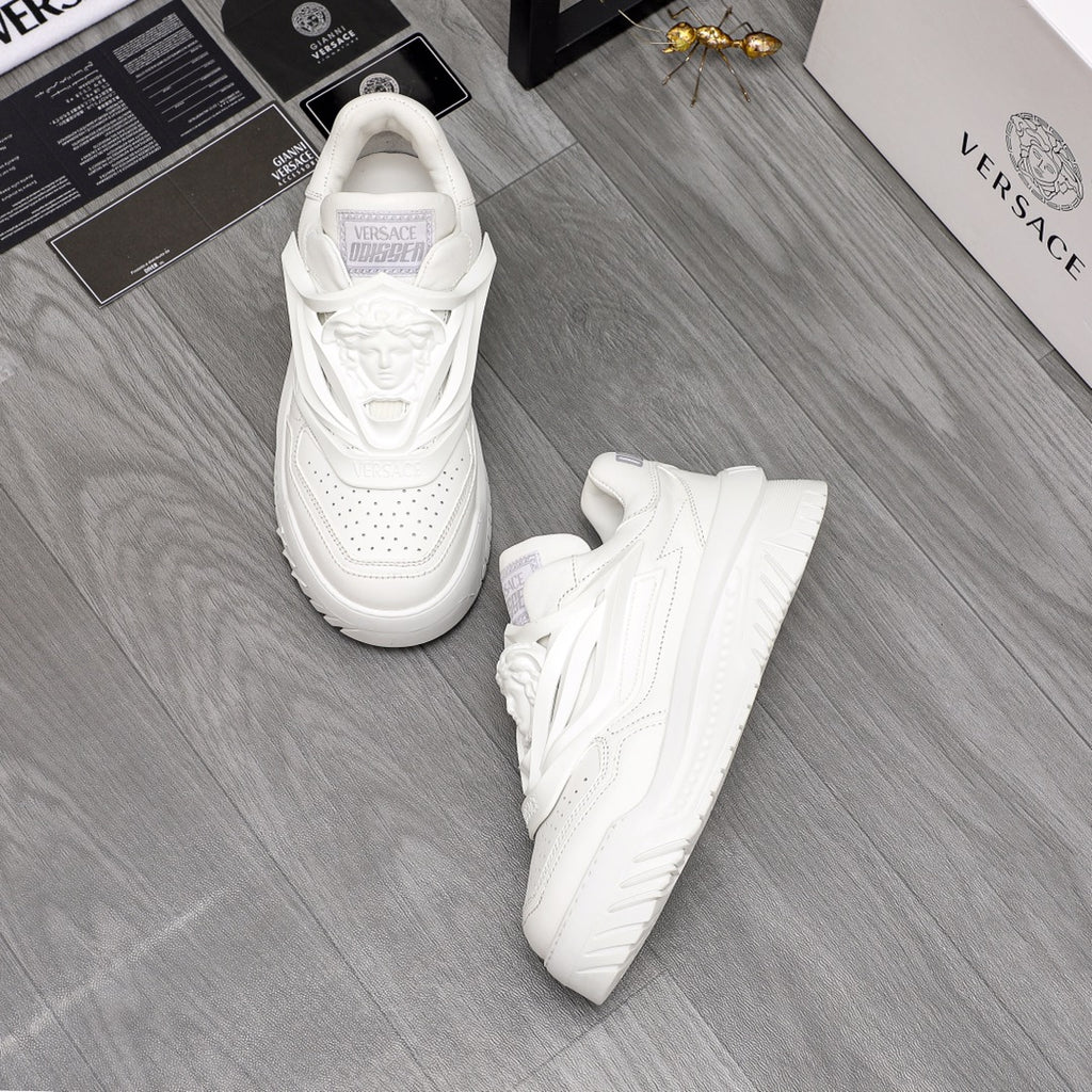 Pair of white Versace sneakers with lace-up front and chunky outsole on the floor.