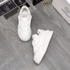 Pair of white Versace sneakers with lace-up front and chunky outsole on the floor.