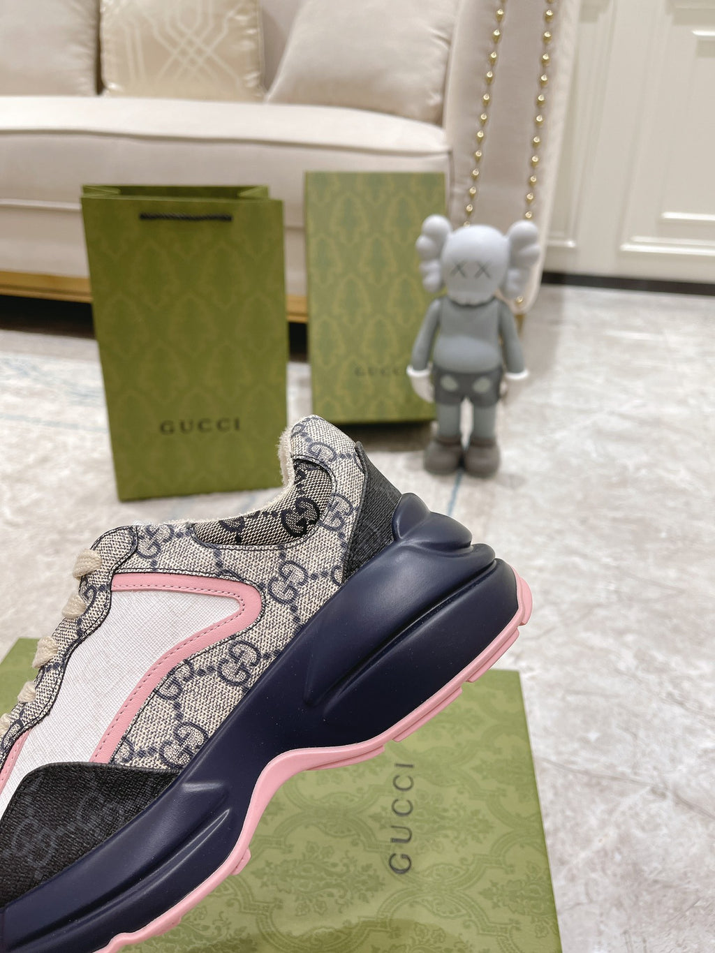 Gucci unisex sneakers close-up, GG canvas upper with pink trim and thick navy sole.