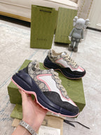Gucci unisex sneakers held in hand, GG print upper with pink trim and dark navy sole.