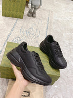 Dark/black Gucci lace-up sneakers held in hand, chunky sole and side panel seams