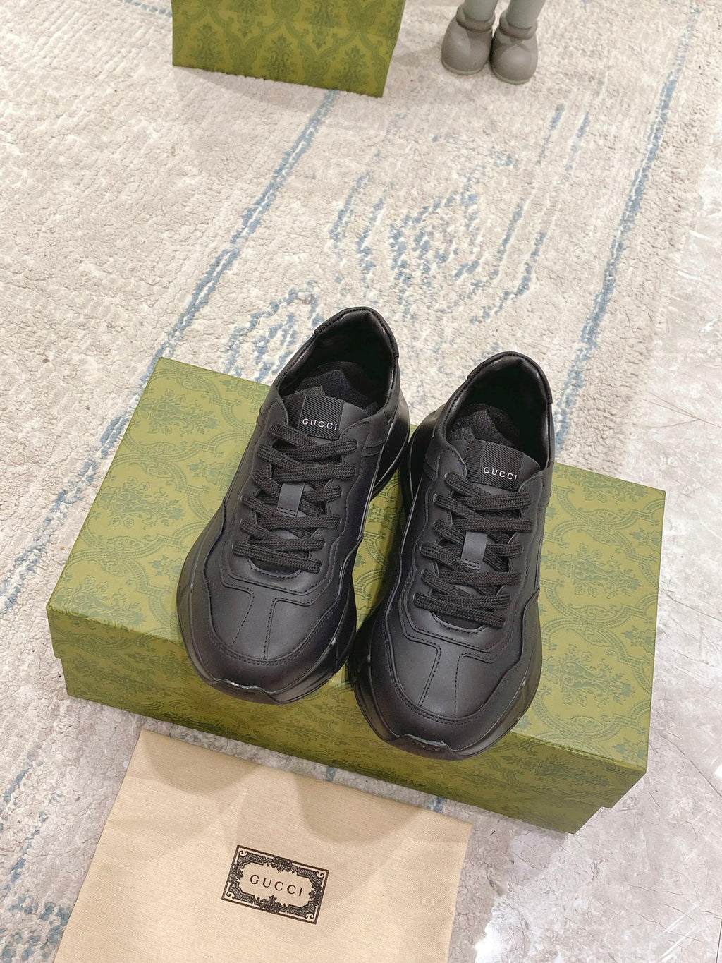 Dark/black Gucci lace-up sneakers, two shoes on green box with visible tongue logo