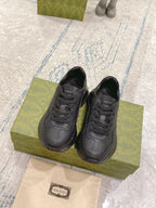 Dark/black Gucci lace-up sneakers, two shoes on green box with visible tongue logo