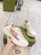 White Gucci unisex sneakers held in hand, showing multicolor LOVE PARADE side text