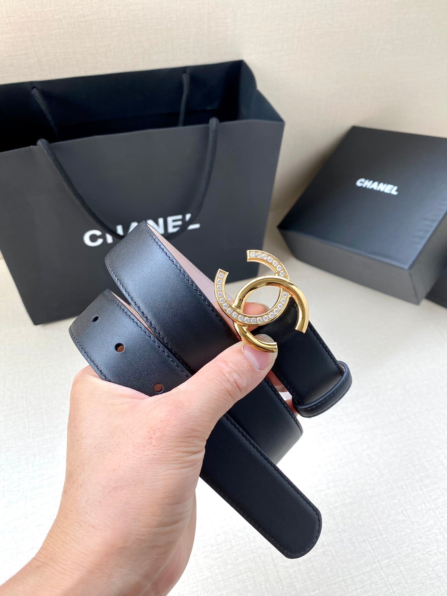 Chanel leather belt with dark blue strap and gold CC buckle, held in hand