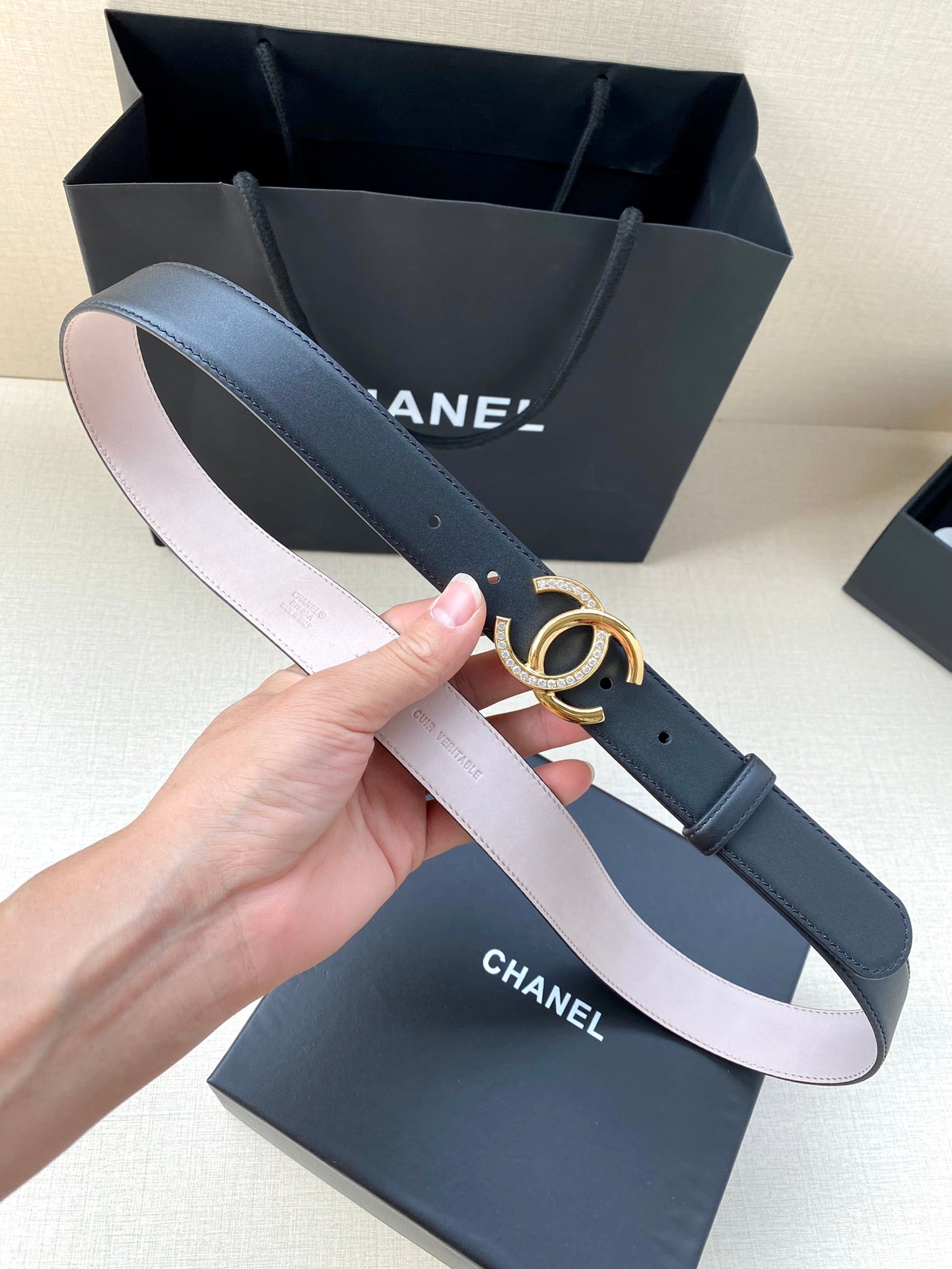 Chanel leather belt in dark blue with gold CC buckle, held next to box