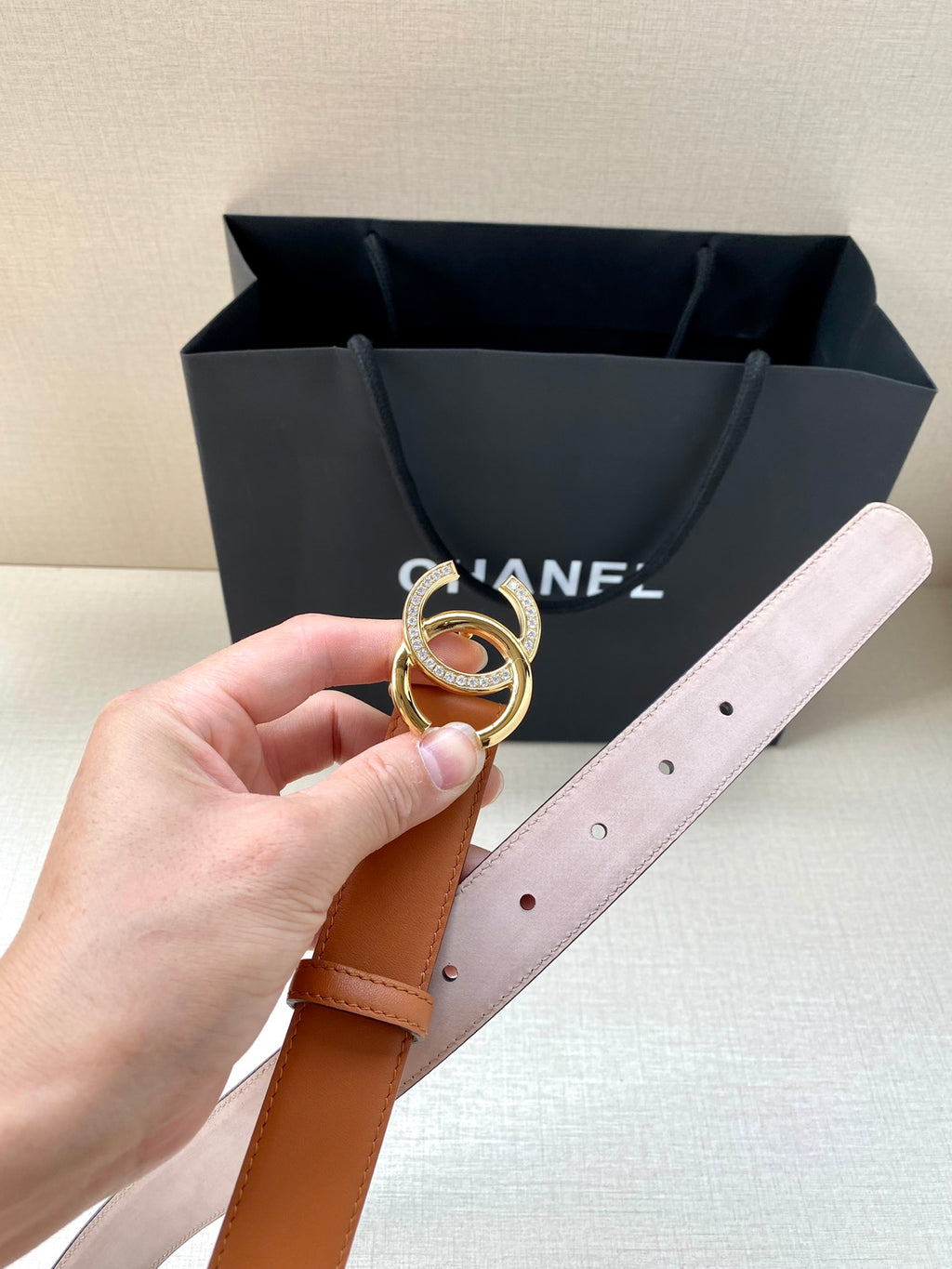 Orange leather belt with gold double-C buckle and pale strap edge, held up to camera