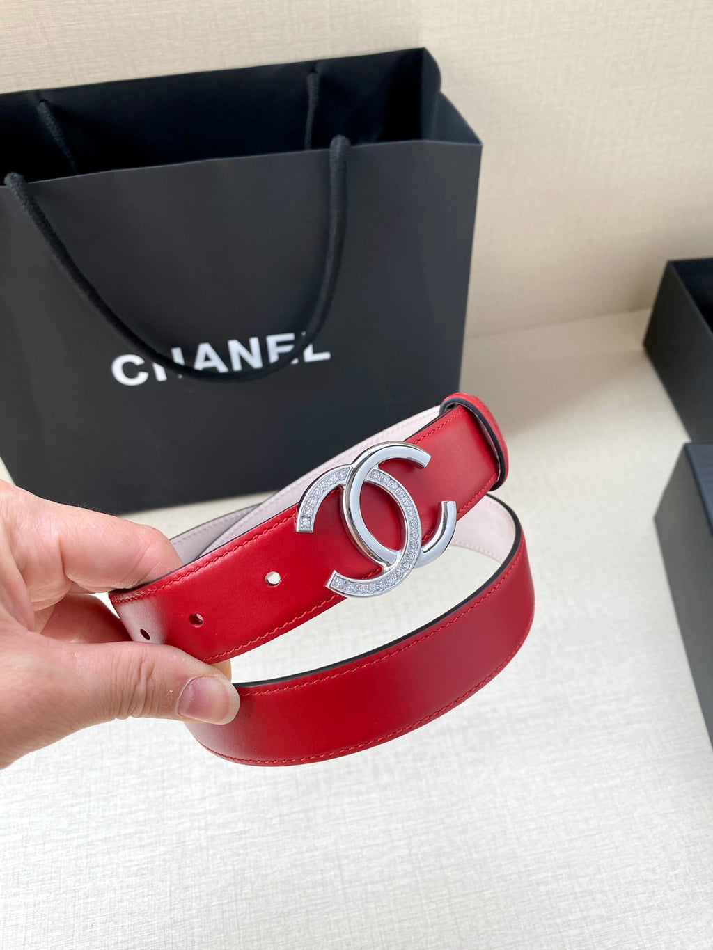 Red leather belt with silver-tone CC buckle, light pink underside, end with pin holes.