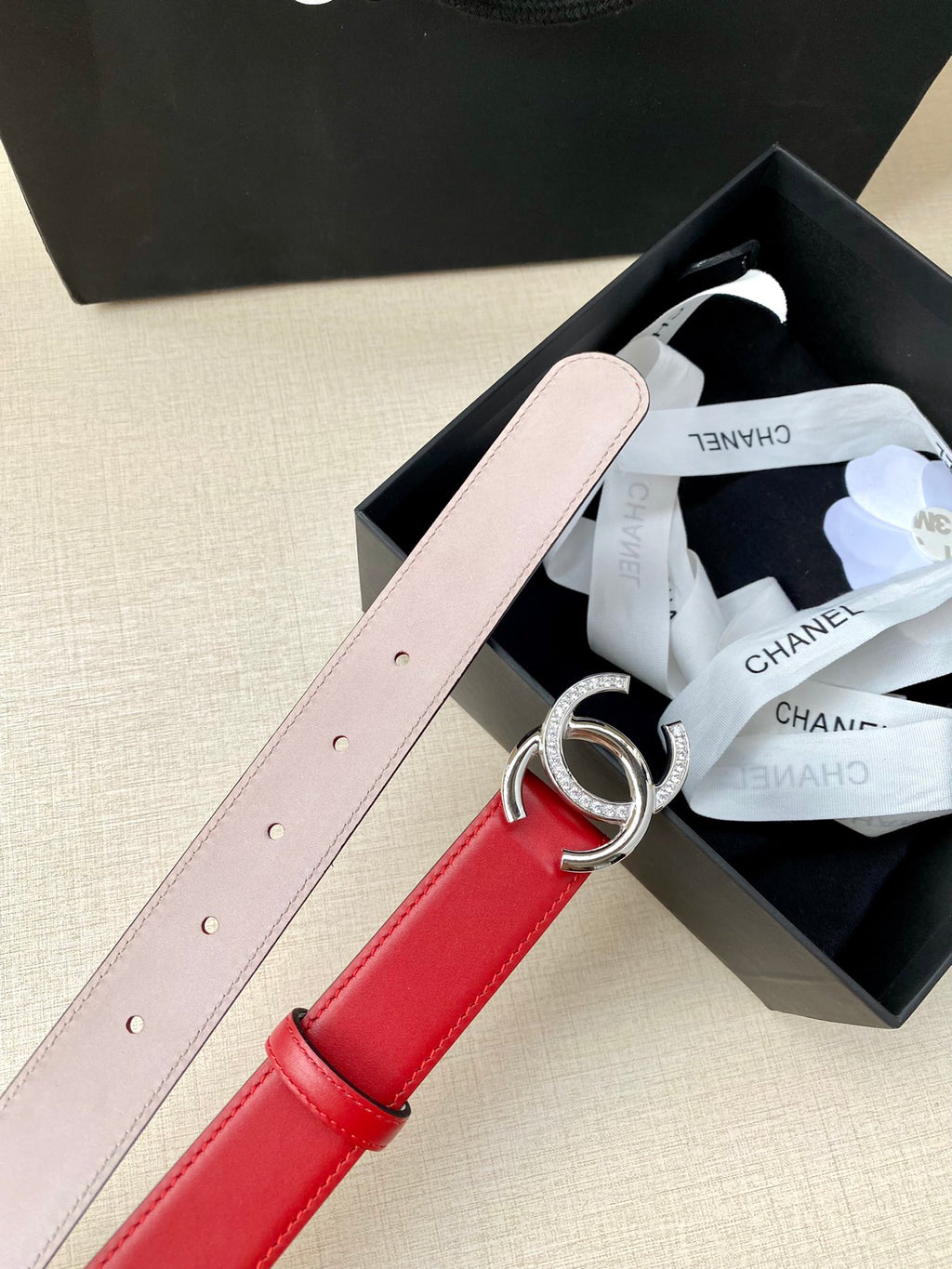 Red leather belt with silver-tone CC buckle, light pink strap, adjustable pin holes.