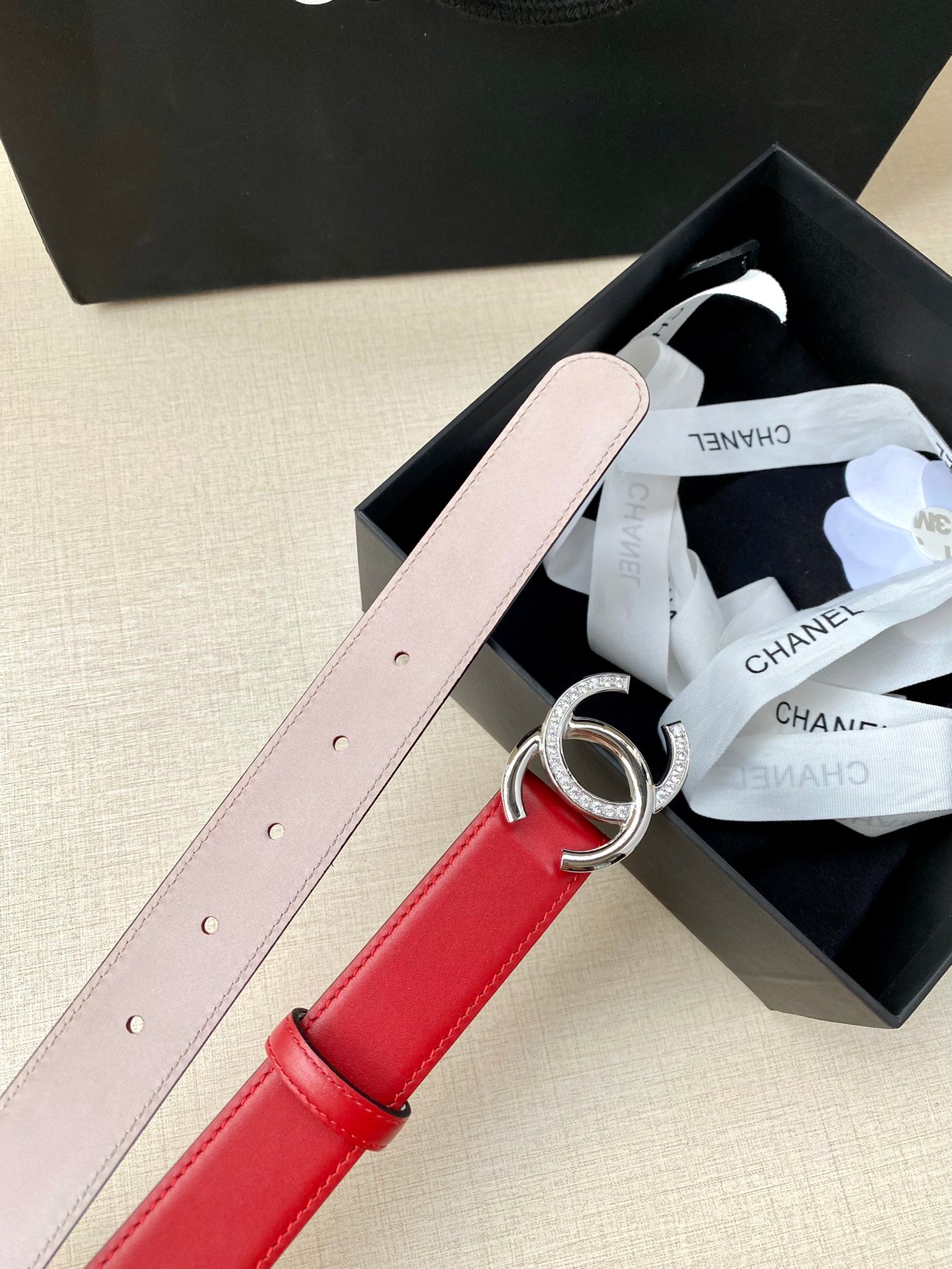 Red leather belt with silver-tone CC buckle, light pink strap, adjustable pin holes.