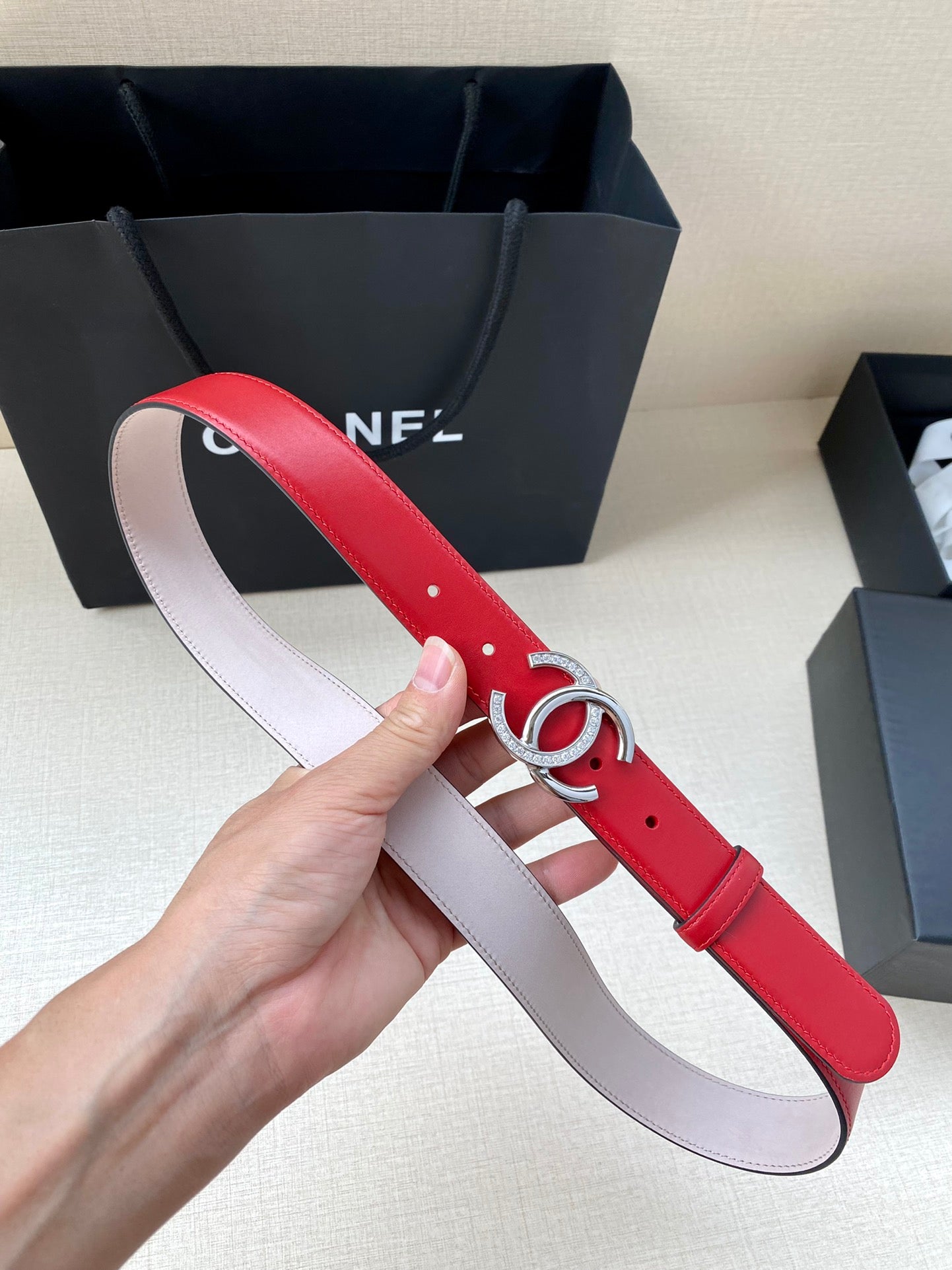 Red leather belt with silver-tone CC buckle, light pink underside, pin holes visible.
