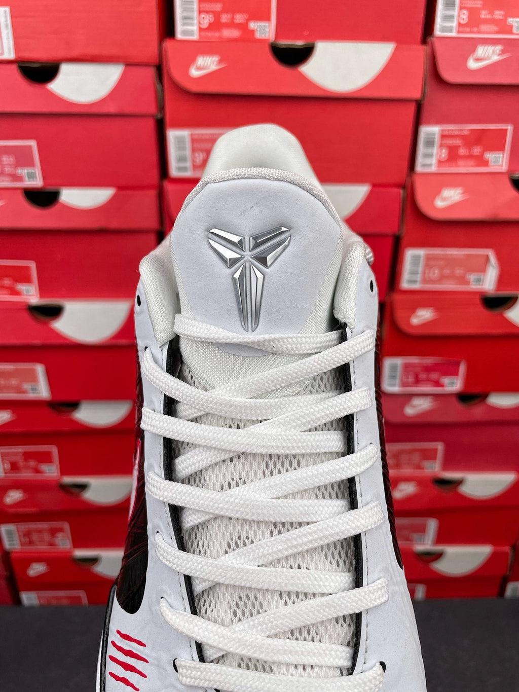 White high-top sneakers with white laces and silver Kobe-style emblem on heel